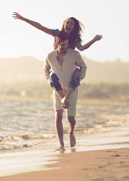 A guy carrying a girl on his back at the beach outdoors